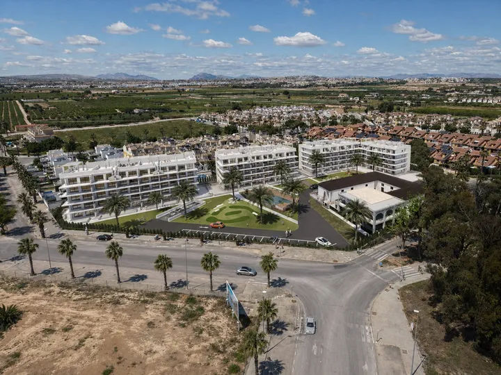 Luftbild-Visualisierung von Oasis Garden in El Raso: die Wohngebäude, die Gärten mit Minigolf und der Pool, dahinter Felder und Hügel